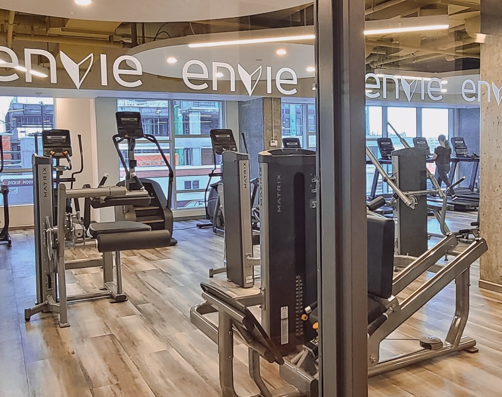 View of fully equipped fitness centre through a window with the Envie logo