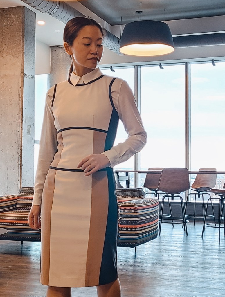 Young woman in dress and collared shirt standing in suite with 29th floor city view in front of dining and lounge area